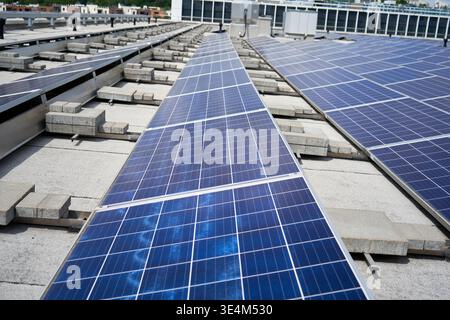Reihen blauer Photovoltaik-Solarpaneele auf einem flachen Dach des Geschäftsgebäudes. Die Solar-Arrays sind mit Betonballastblöcken montiert Stockfoto