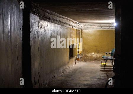 Ein schwach beleuchteter unterirdischer Keller- oder Kellerkorridor mit rauen, feuchten Betonwänden mit sichtbaren Feuchtigkeitsschäden und dunklen Flecken. Der Raum Stockfoto