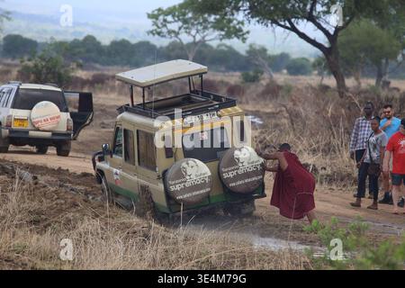 Ein Maasai-Mann hilft, ein Safari-Fahrzeug im Schlamm zu schieben, Tansania, Ostafrika Stockfoto