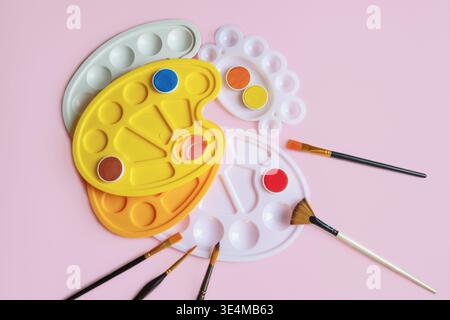 Verschiedene Paletten, Aquarellfarben und Pinsel auf rosa Hintergrund. Flache Ladefläche, Kopierraum Stockfoto