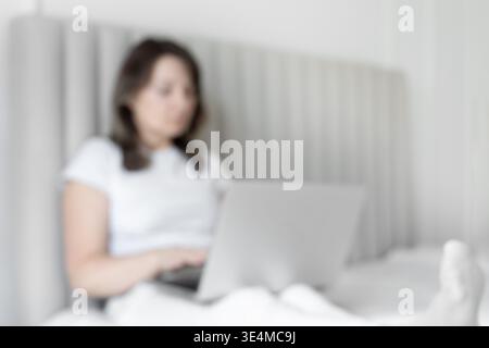 Verschwommene Frau, die zu Hause im Bett am Laptop arbeitet Stockfoto