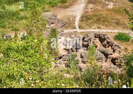 Ein malerischer Blick auf eine felsige Landschaft mit großen verwitterten Felsblöcken und zerklüfteten Steinformationen, umgeben von üppiger grüner Vegetation. Im Stockfoto