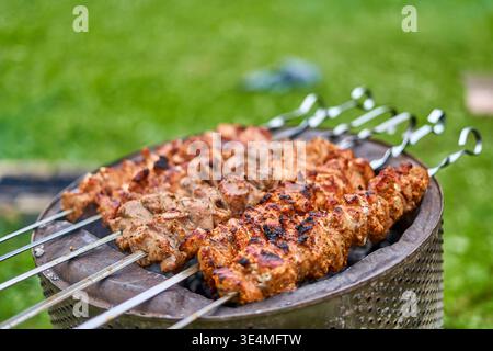 Gegrillte Fleischspieße, die auf einem traditionellen runden Holzkohlegrill im Freien kochen. Mehrere Metallspieße halten mariniertes Fleisch Stockfoto