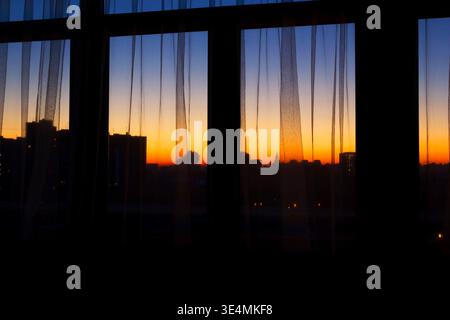 Skyline der Stadt Moskau bei Sonnenuntergang, Blick durch Fenstervorhänge aus dem Inneren des Apartments Stockfoto