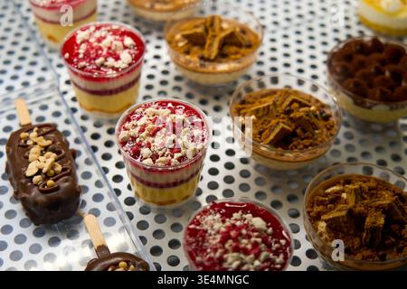 Verschiedene Gourmet-Desserts in Plastikbechern und Schokoladentafeln auf einem Stock. Auswahl an Panna Cotta, Tiramisu und Kuchen in einer Konditorei. Stockfoto
