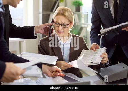 Überarbeitete Geschäftsfrau unter Druck mit Papierkram und Telefonen am Schreibtisch Stockfoto
