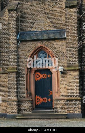 Nahaufnahme eines historischen Kircheneingangs mit einer kunstvollen gotischen Holztür, dekorativen Metallelementen und einer alten Ziegelmauer. Architektonische Details der Tradition Stockfoto