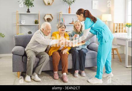 Die Pflegefachkraft serviert Tee für lächelnde Senioren, genießt warme Getränke und freundliche Gespräche. Stockfoto