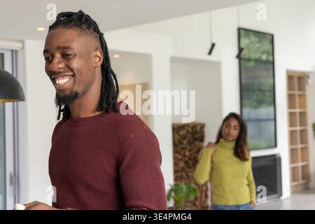 Diverse Paare teilen sich morgens im Wohnzimmer, Mann lächelt und hält eine weiße Tasse in der Nähe des Kamins Stockfoto