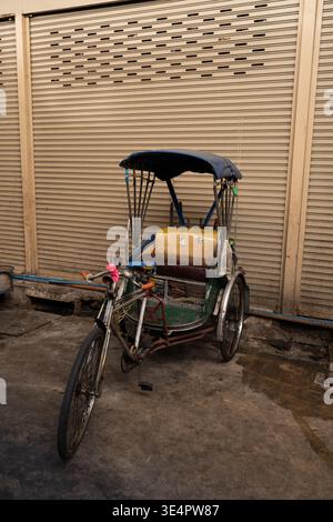 Bangkok Thailand 25. Januar 2026. Fahrrad-Rikscha parkt in der Nähe geschlossener Metallläden in der Samut Prakan District Street. Stockfoto