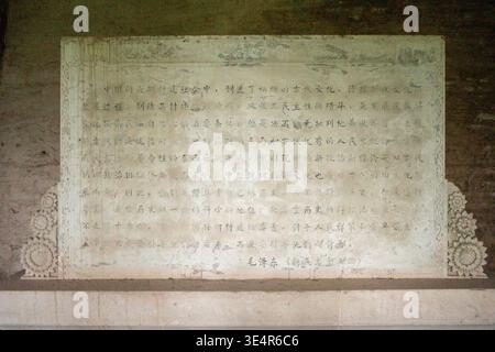 Verwitterte Steintafel mit graviertem Text und dekorativen Borten. Geschnitzte Zeichen, die in klaren horizontalen Linien angeordnet sind. An strukturierter Wand montierte Plakette Stockfoto