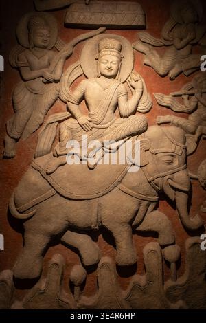 Buddhistische Gottheit reitet auf Elefanten in Steinrelief. Elegante Schnitzereien zeigen heitere göttliche Präsenz. Elefantendetails in traditioneller Handwerkskunst. W Stockfoto