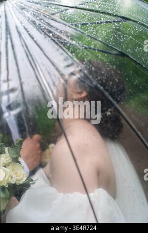 Wunderschönes Hochzeitspaar, das sich unter einem Regenschirm im Wald umschließt. Stilvolle Küsse für Braut und Bräutigam. Unscharfer Hintergrund. Stockfoto
