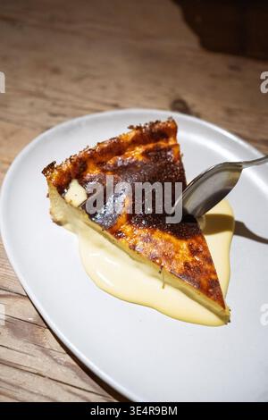 Baskischer Käsekuchen mit verbrannter Oberseite auf einem weißen Teller mit cremiger Puddingsoße Stockfoto