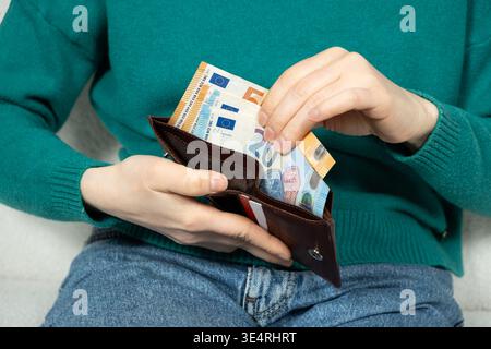Die Hände legen die Euro-Banknoten in die Brieftasche. Konzepte der finanziellen Sicherheit, Liquidität und wirtschaftlichen Stabilität mit Papierwährung. Stockfoto