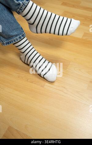 Nahaufnahme der Füße mit gestreiften Socken. Person, die die Beine auf Holzboden kreuzt. Stockfoto