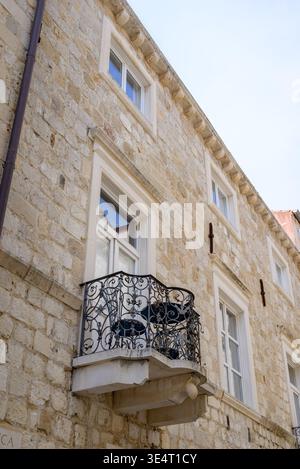 Steinfassade mit weiß gerahmten Fenstern und einem kunstvoll verzierten schmiedeeisernen Balkon, von unten aus vor einem klaren blauen Himmel, mediterrane Geschichte Stockfoto