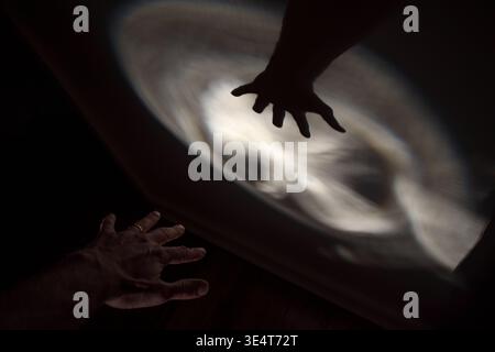 Eine Hand und ihr Schatten greifen in einem Kreis aus Licht vor dunklem Hintergrund zueinander. Stockfoto