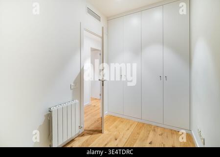 Ein modernes, minimalistisches Interieur eines Zimmers mit weißen Wänden und Holzfußboden. Eine geschlossene Tür führt zu einem anderen Raum, und ein Kühler ist auf dem sichtbar Stockfoto