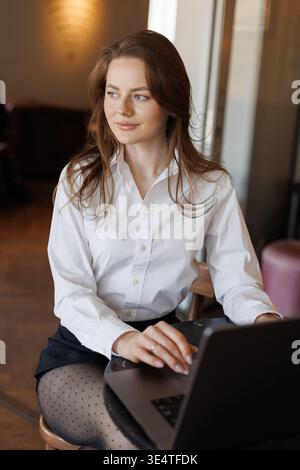 Freiberuflicher Mitarbeiter bei der Arbeit in einem gemütlichen Café. Frau in elegantem Outfit auf einem Laptop, umgeben von modernen Grundausstattung wie Kaffee, Notebook und Telefon. Stockfoto