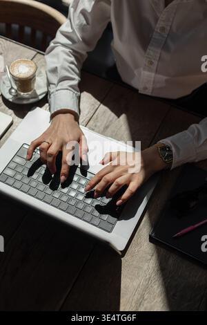 Blick von oben auf eine professionelle Frau, die von einem gemütlichen Café aus mit Kaffee, Smartphone und Planer arbeitet. Frau, die in sonnendurchfluteter Umgebung am Laptop arbeitete Stockfoto
