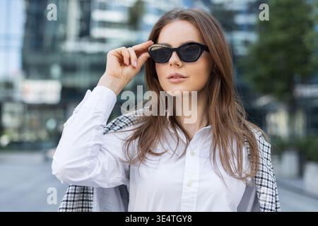 Selbstbewusste Geschäftsfrau in trendiger Büromode im Stadtzentrum mit Glasgebäuden. Moderne Stadtfrau in modischer Kleidung und Stockfoto