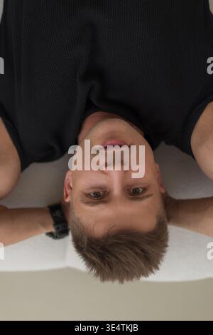 Schöner erfolgreicher Geschäftsmann mit Haarfrisur in schwarzem T-Shirt liegt auf dem Sofa und schaut in die Kamera, Draufsicht. Cooler Kerl Stockfoto