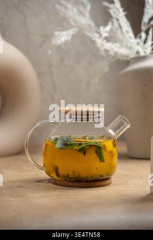 Kräutertee mit Pfefferminze in Glas-Teekanne auf dem Tisch Stockfoto