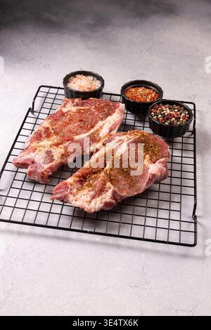 Rohe Schweinefleisch-Steaks auf einem Grillregal, gewürzt mit gemischten Gewürzen, grobem Salz und Pfeffer, bereit zum Marinieren und Grillen Frische, saftige Schnitte für ein Fass Stockfoto