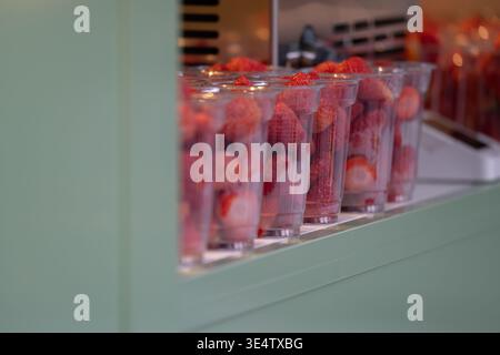 Frische Erdbeeren in durchsichtigen Plastikbechern, die im Einzelhandel oder auf der Straße ausgestellt werden. Helle, natürliche Produktpräsentation mit Fokus auf Stockfoto
