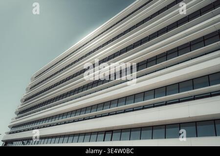 Moderne weiße Gebäudefassade mit schlanken horizontalen Linien und dunklen Glasfenstern, aus einem niedrigen Winkel vor klarem Himmel fotografiert, was minimalistisch wirkt Stockfoto
