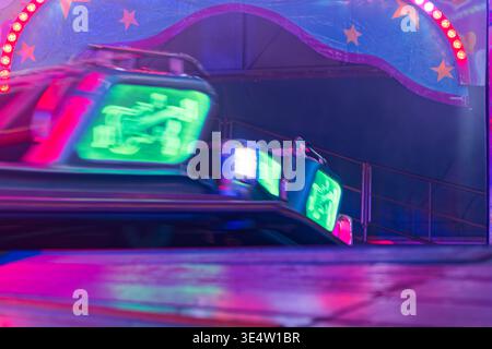 Leuchtende Stoßfängerautos, die von neongrünen und rosa Lichtern beleuchtet werden, sorgen für eine lebendige Karnevalsszene mit Bewegungsunschärfe und Sternendekorationen im Hintergrund. Stockfoto