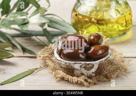 Essen, Feinkost griechische Kalamata schwarz rot glänzende Oliven in Keramikschale auf Holztisch. Öl und Zweige. Selektiver Fokus Stockfoto