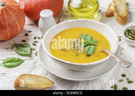 Essen, vegetarische Kürbiscreme-Suppe-Püree mit Olivenöl, Samen und Basilikum auf einem hellen Holztisch auf einem weißen Teller. Selektiver Fokus Stockfoto