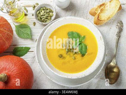 Essen, vegetarische Kürbiscreme-Suppe-Püree mit Olivenöl, Samen und Basilikum auf einem hellen Holztisch auf einem weißen Teller. Selektiver Fokus Stockfoto