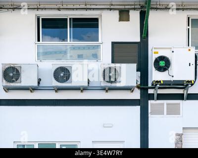 Gebäudeaußenwand mit mehreren montierten Klimaanlagen, einschließlich Kompaktkondensatoren und einem größeren industriellen System. Stockfoto