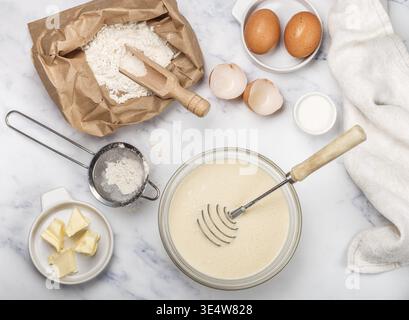 Essen, Zubereitung von Teig für hausgemachte Pfannkuchen zum Frühstück. Zutaten auf dem Tisch - Weizenmehl, Eier, Butter, Zucker, Salz, Milch. Selektiver Fokus Stockfoto