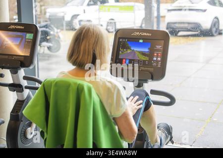 Eine Frau trainiert auf einem Heimtrainer vor einem großen Fenster, Fitness TSV Calw, Deutschland Stockfoto