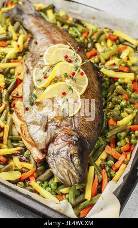 Essen, gebackene Fischforelle mit Gemüse (Kartoffeln, Karotten, Bohnen, grüne Erbsen und Zwiebeln) mit Zitrone, Thymian und rosa Pfeffer. Wildlachs. Feinkost Stockfoto