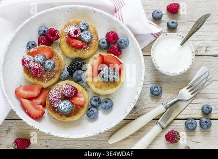 Essen, Hüttenkäsepfannkuchen, Syrniki, Quark-Krapfen mit frischen Beeren (Himbeere, Erdbeere, Heidelbeere, Brombeere) und Puderzucker in einem weiß Stockfoto