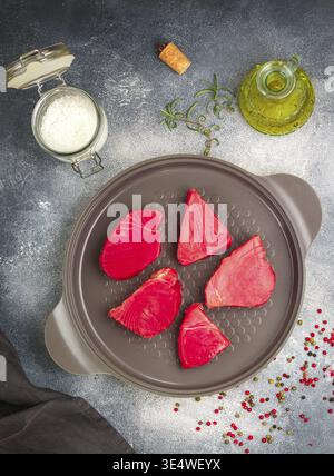 Speisen, rohe Thunfisch-Steaks mit Meersalz, rosa, grünem und schwarzem Pfeffer und Rosmarin zum Grillen oder Kochen in einer gusseisernen Pfanne. Bereiten Sie ein köstliches Abendessen zu Stockfoto