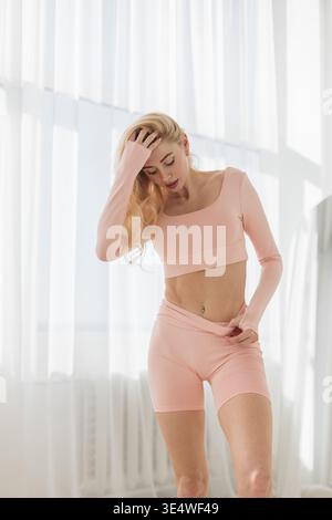 Selbstbewusstes junges weibliches Model in pastellfarbener Aktivkleidung, das in einem hellen, minimalistischen Innenraum posiert. Stockfoto