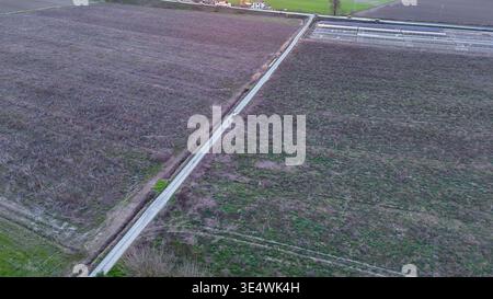 Drohnenblick auf bepflanzte Felder und Gewächshäuser in der fruchtbaren Landschaft von Emilia, mit einem Radfahrer, der auf einer Landstraße in Richtung Horizo fährt Stockfoto