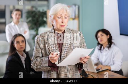 Traurige ältere Frau, die Dokumente im Amt hält Stockfoto