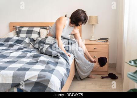 Frau, die morgens aus dem Bett steigt und warme Hausschuhe anzieht. Beginnen Sie den Tag und fühlen Sie sich wie zu Hause. Authentischer Lifestyle Stockfoto