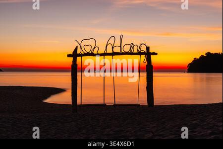 Blick auf den Sonnenuntergang mit Koh Adang Schild am Strand. Ruhiges Meer und lebendiger Himmel. Silhouette aus Schaukeln und tropischer Insellandschaft. Stockfoto
