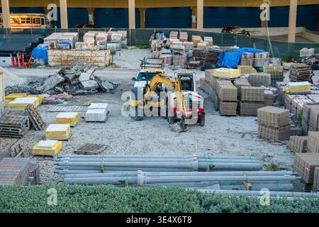 Ein organisiertes Baustofflager verfügt über Stapeln von Pflastersteinen, Betonbarrieren und einen Bagger auf einer Baustelle. Stockfoto