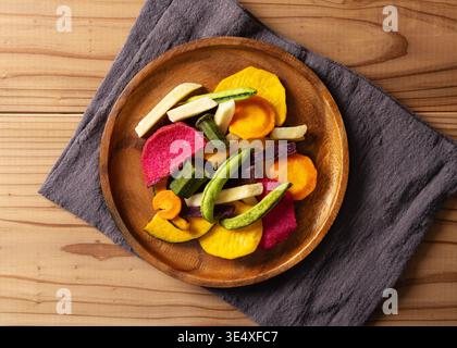 Blick von oben auf verschiedene bunte Gemüsechips auf einem Holzteller mit einer Leinenserviette, flach gelegen Stockfoto