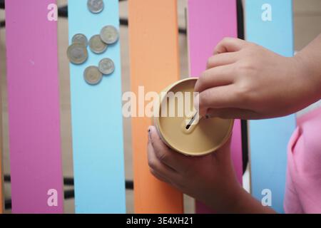 Das Kind speichert Münzen in einem Behälter auf einem farbenfrohen Tisch Stockfoto