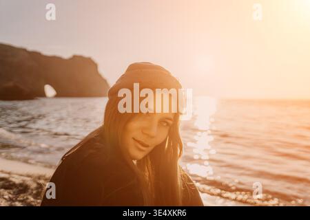 Frau, Beanie, Sonnenuntergang, attraktive Frau in Beanie blickt zurück auf den Strand während eines wunderschönen orangen Sonnenuntergangs Stockfoto